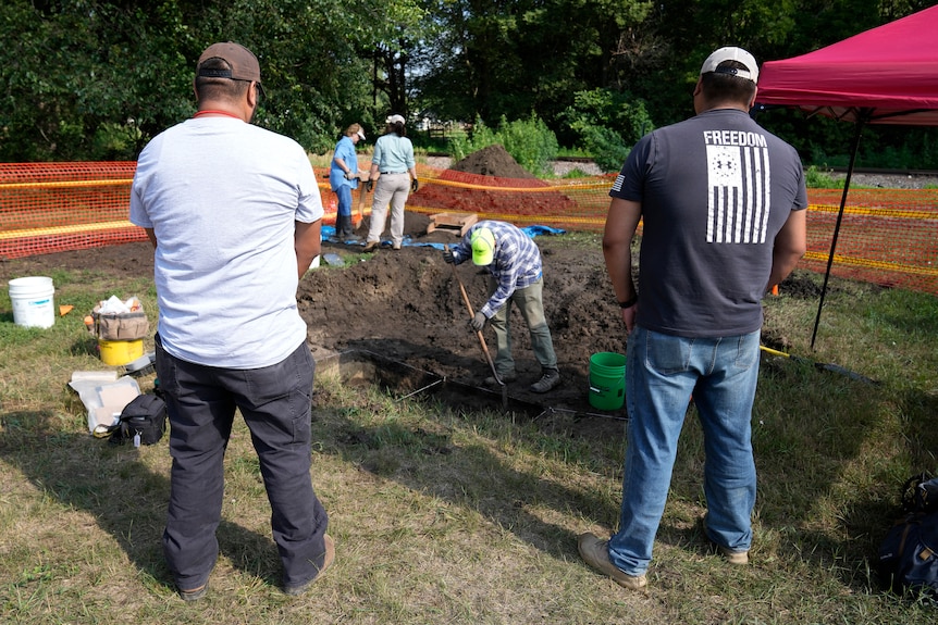 People stand around an excavation site. 