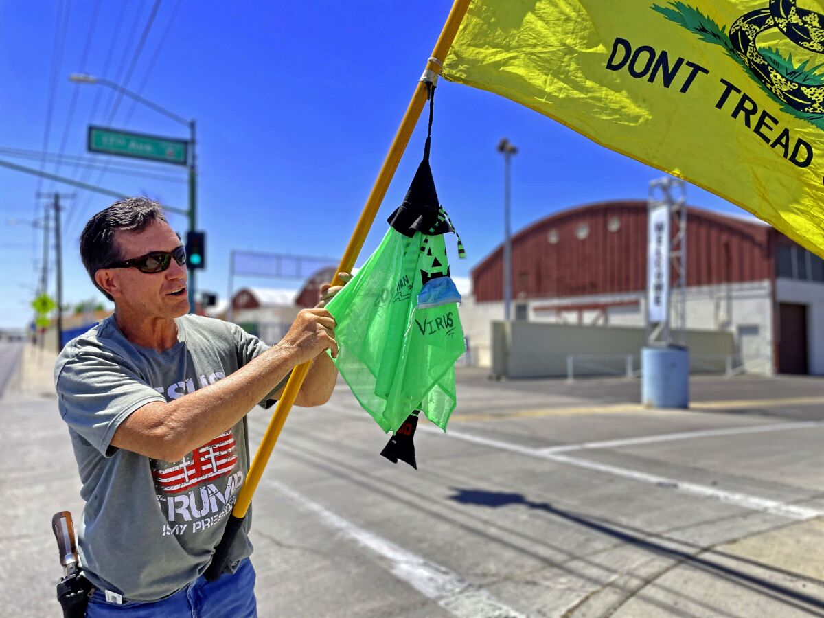 A man in a Trump shirt with a gun on his hip waves a "Don't Tread On Me" flag