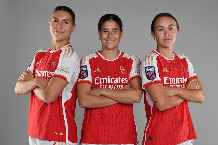 Three women soccer players wearing red and white cross their arms for a portrait photo