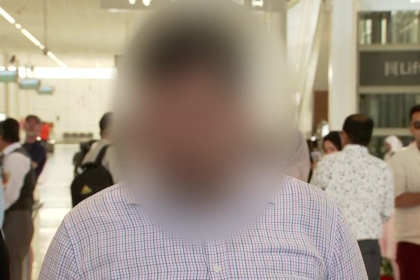 A man wearing a checked button up shirt facing the camera, with his face blurred.