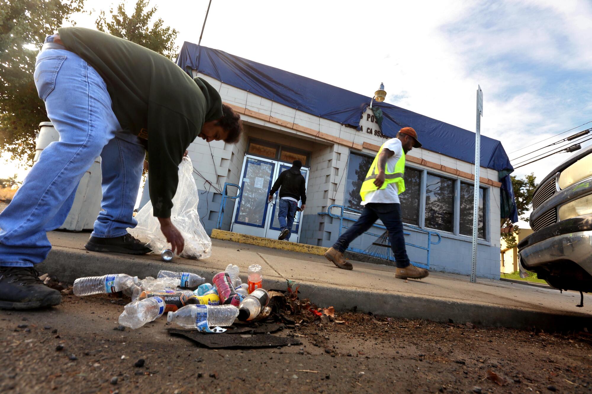 Men pick up debris in front of a post office.