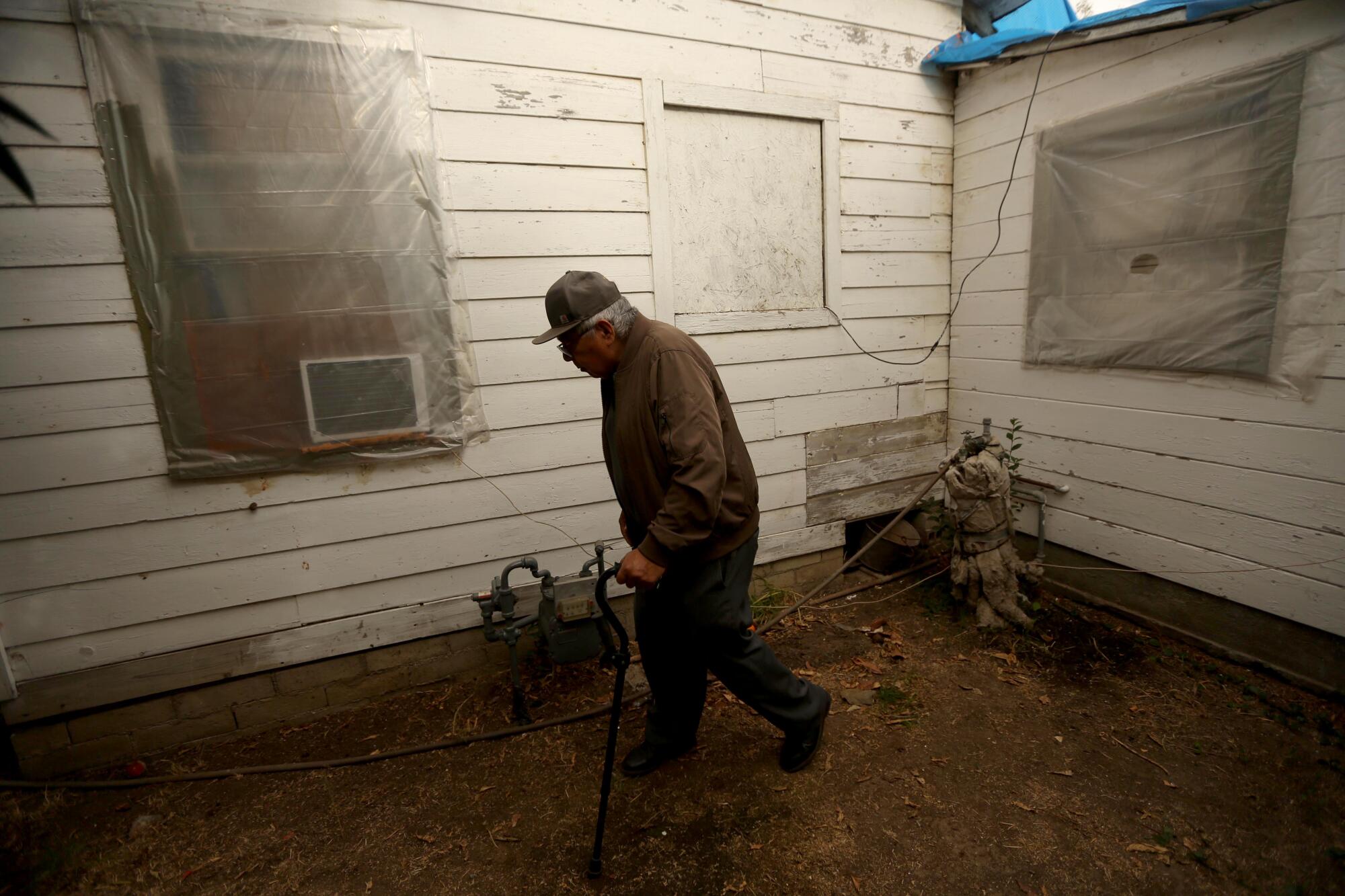 A man walks with a cane outside a flood-damaged home.