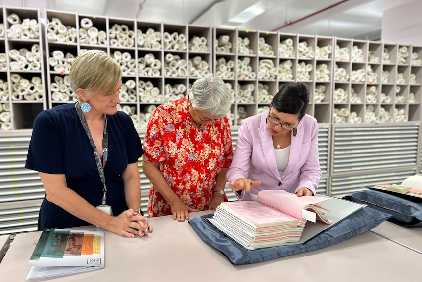 Leanne Enoch pointing at a thick book while Ruth Kerr and Louise Howard watch on.