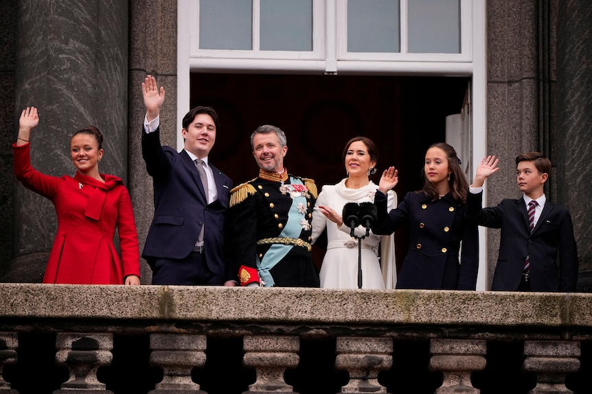 King Frederik and Queen Mary stand on the balcony with their four children waving.