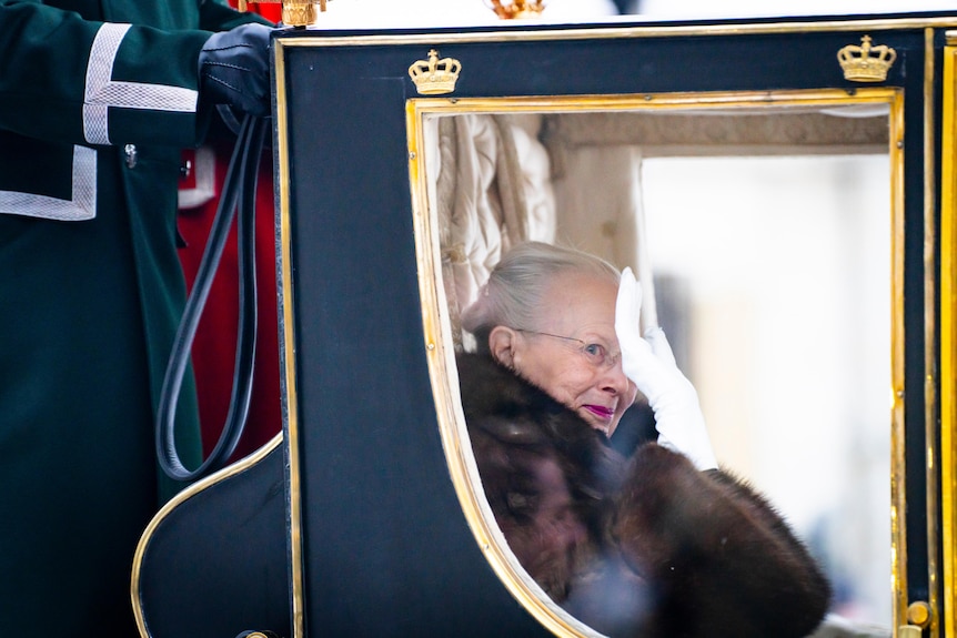 Queen Margrethe sits in a carriage and waves her hand