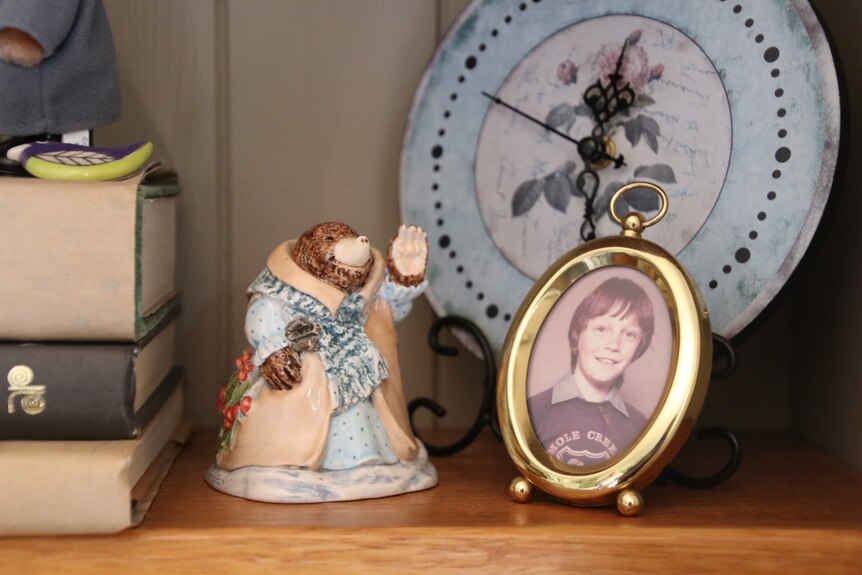 A small ceramic mole dressed in period clothing sits on a shelf next to a portrait of a young child wearing a shirt.