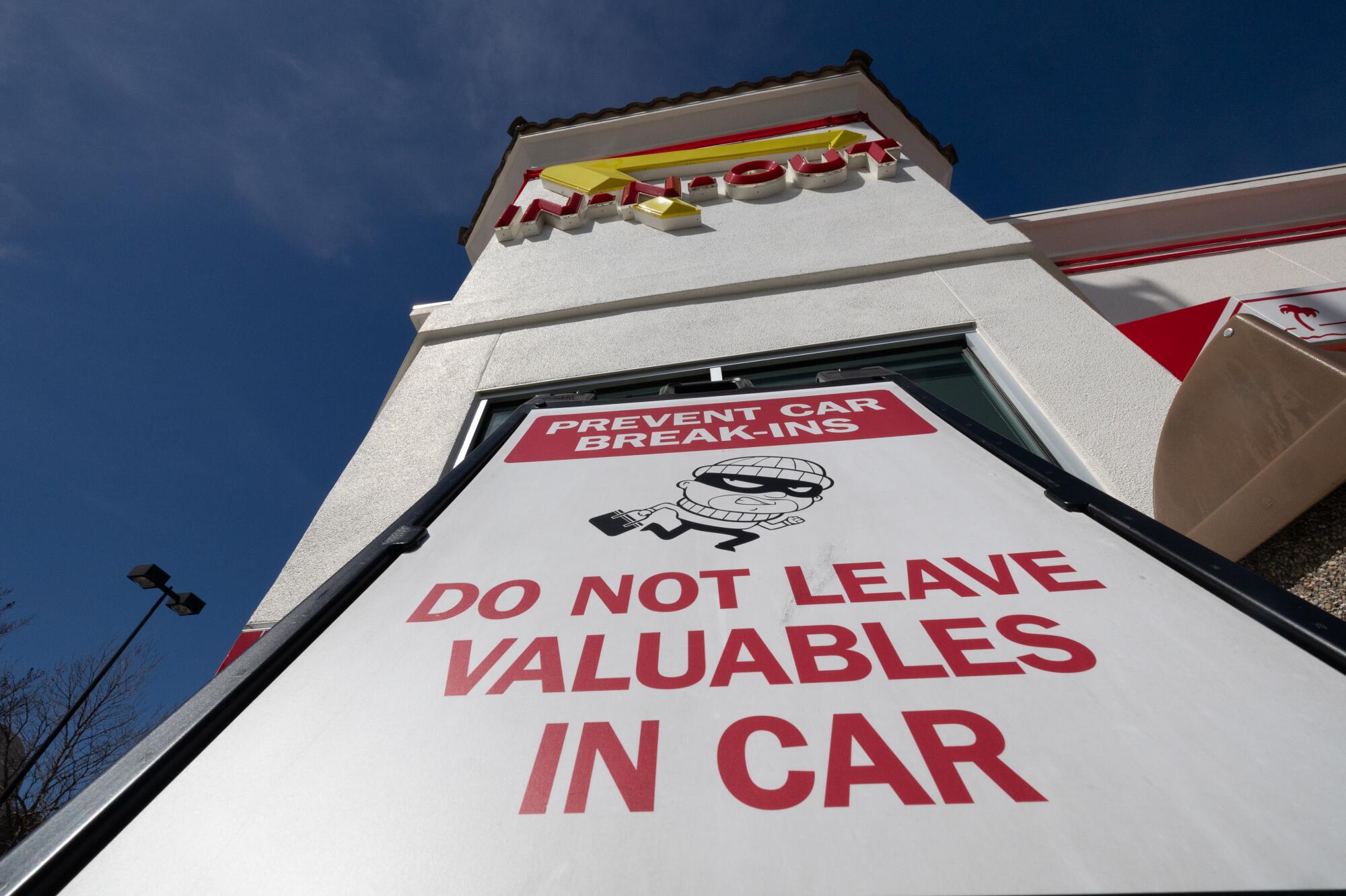 A sign with red lettering reads "Prevent car break-ins/Do not leave valuables in car," with a sketch of a thief in a ski mask