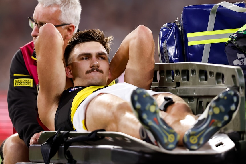 Richmond's Josh Gibcus puts his hands behind his head as he is taken off the AFL field on a medicab.