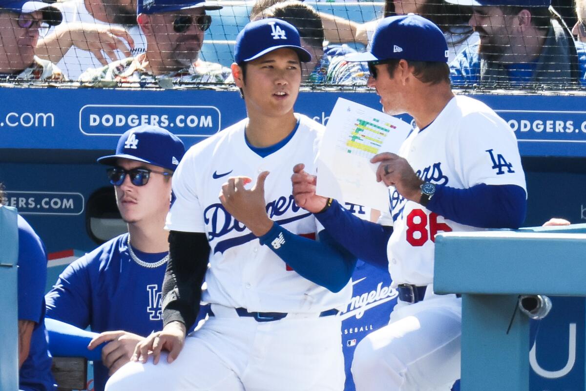 Dodgers star Shohei Ohtani talks with first base coach Clayton McCullough in the dugout.