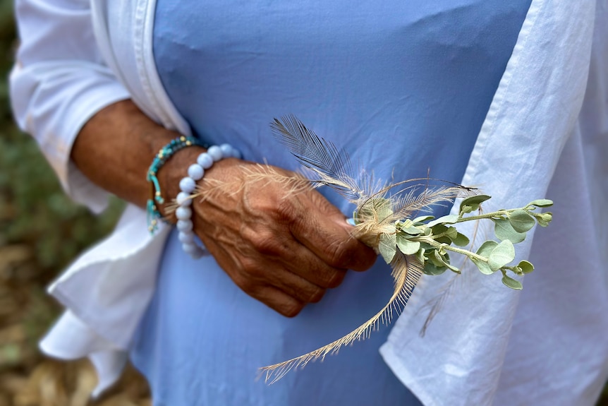 Close up photo of Sophia Pearce's hands, holding a small bunch of salt bush and emu feathers