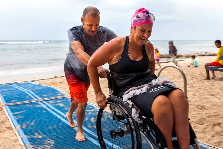 A woman in a wheelchair using Mobi-Matting on a beach.