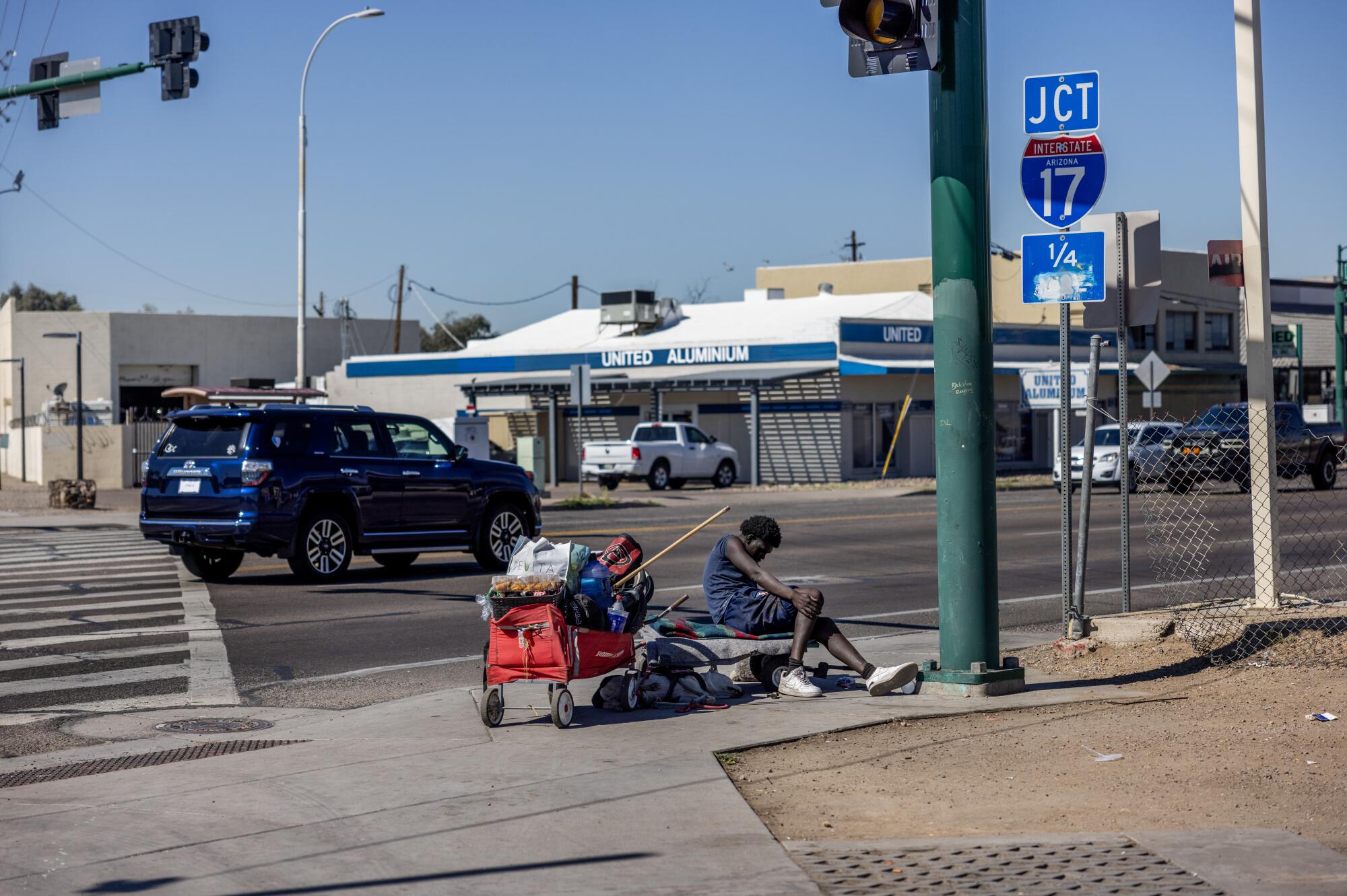 A man with a red cart sitting at an intersection near a freeway sign reading "JCT 17"