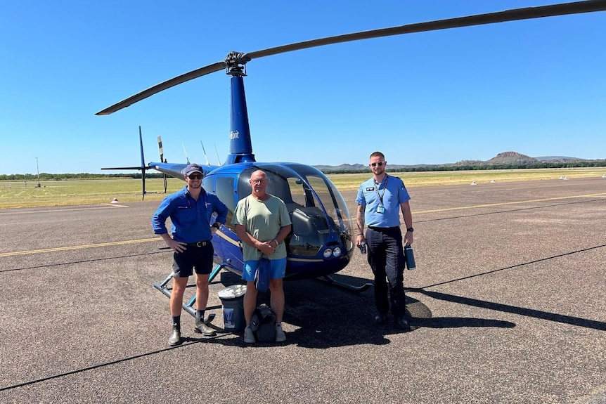 Helicopter pilot and police officer pictured with tourist John Small in front of the helicopter they rescued him in. 