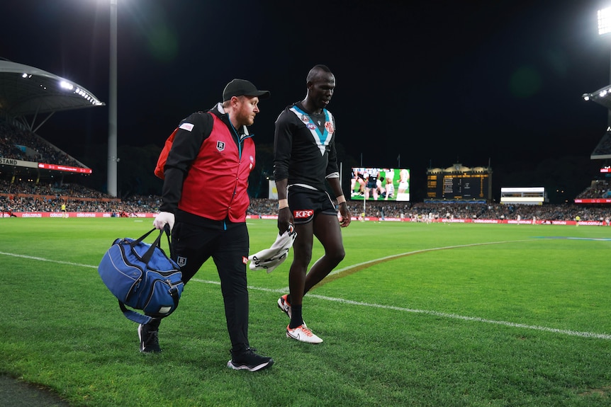 A Port Adelaide defender walks around the boundary with a medical officer after being injured.