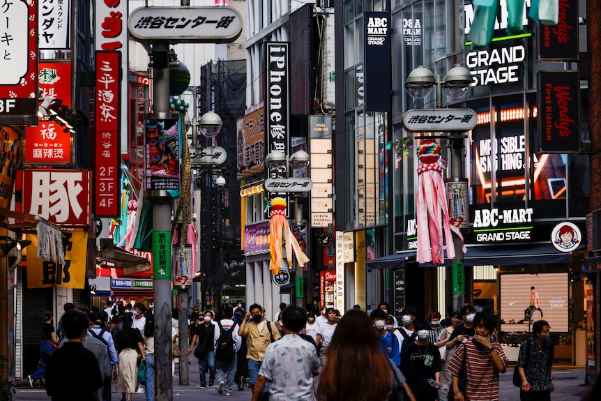 Crowds walk down a street in Japan covered in colourful billboards. 