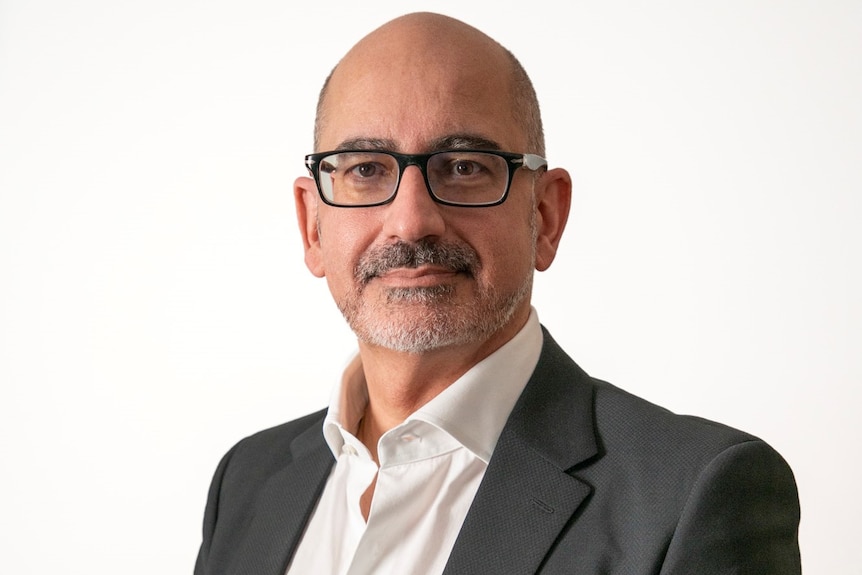 A bald man in his 50s with a goatee, wearing glasses. 