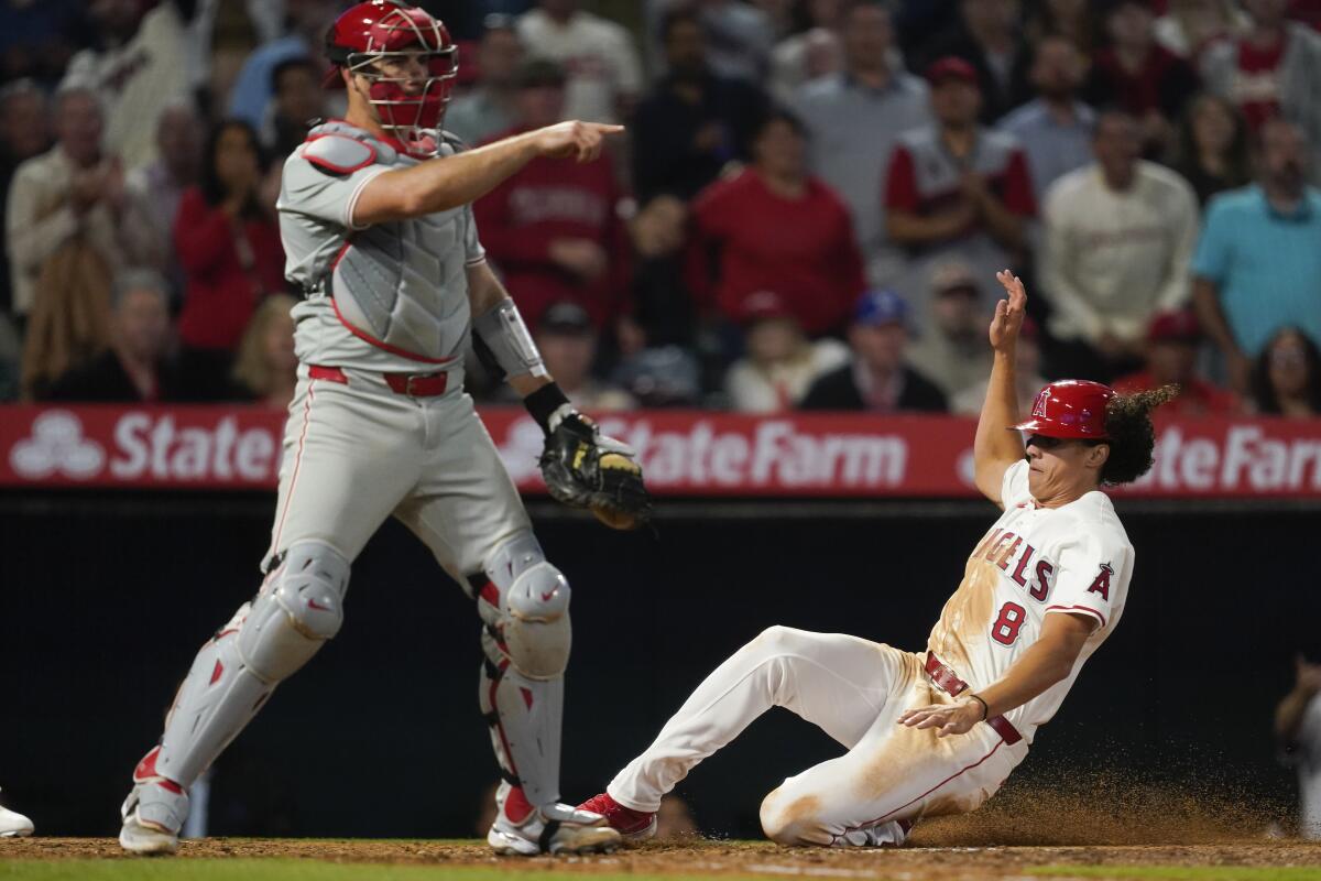 Angels designated hitter Cole Tucker slides past Phillies catcher J.T. Realmuto to score off a double 