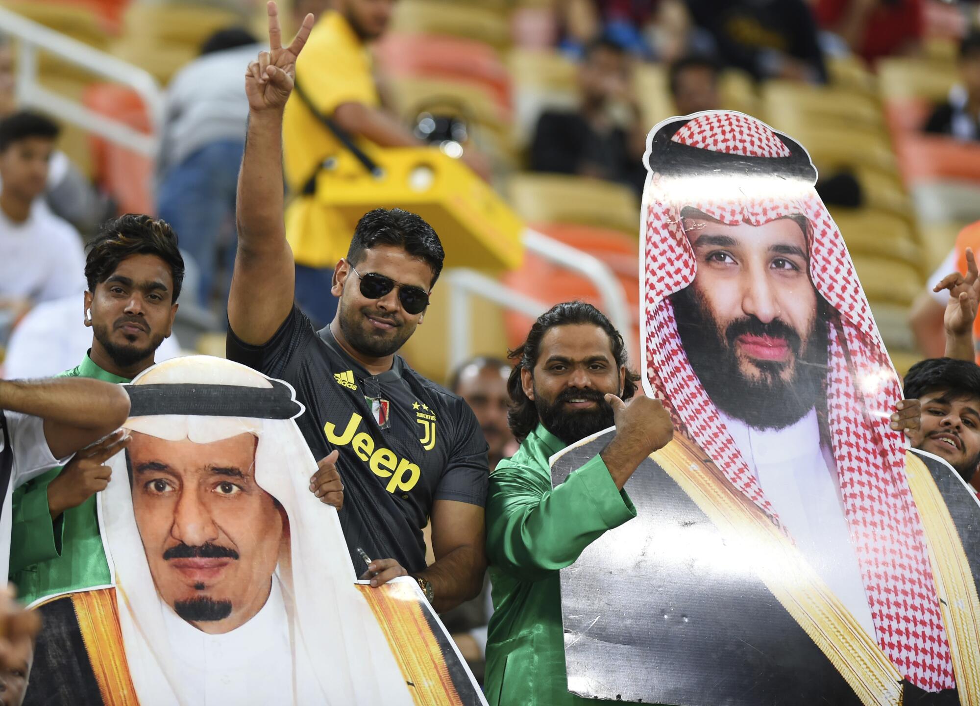 Men hold massive cutout pictures of Saudi Arabia's King Salman and Crown Prince Mohammed bin Salman.