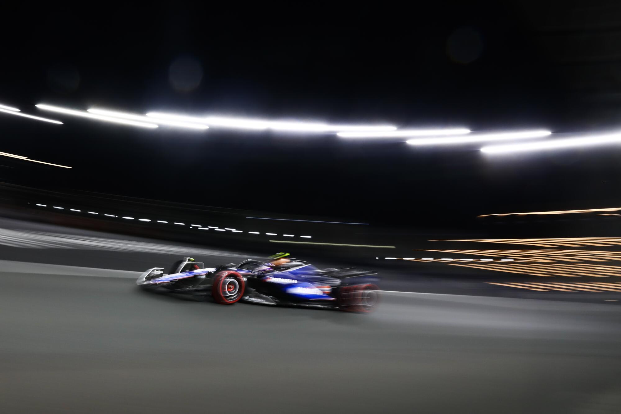 A race car speeds past blurred lights. 