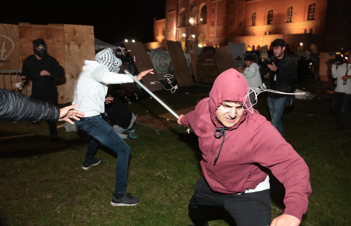A man in a kaffiyeh, left, and a hooded man with a weapon fighting among a crowd at UCLA