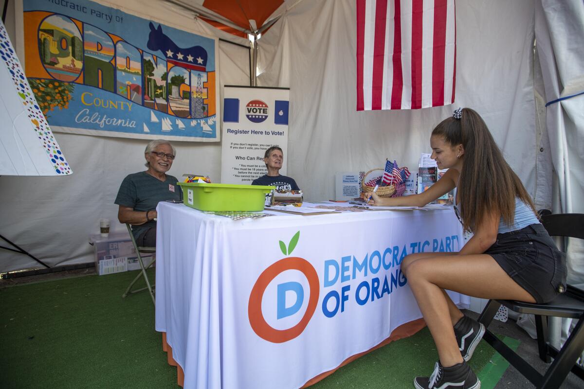 Two volunteers help a woman register to vote at the OC Fair in Costa Mesa.