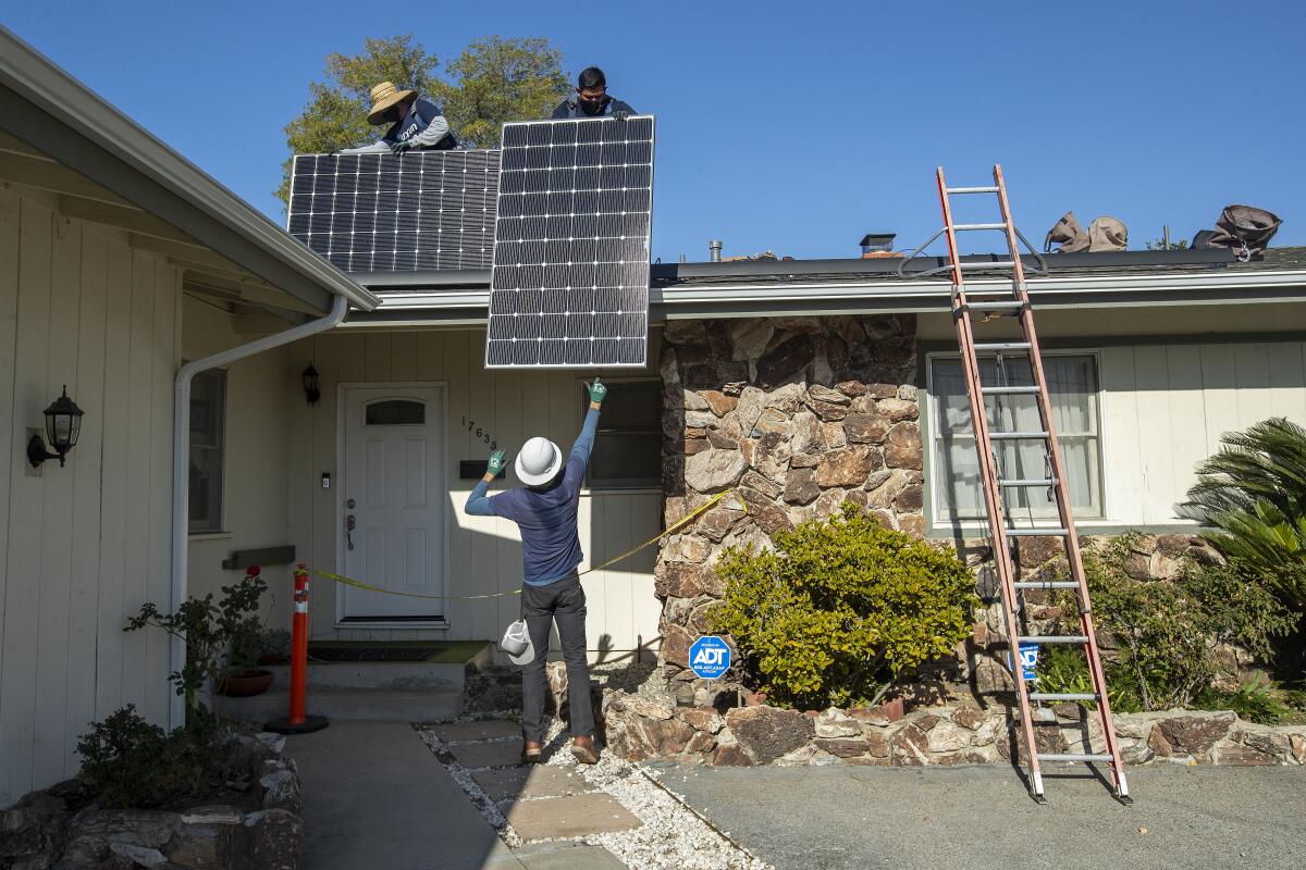 Workers install rooftop solar panels at a house.