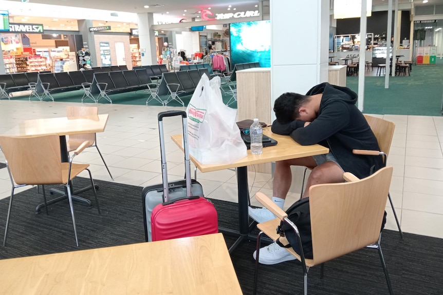 A man sits with his head on the table in the Sunshine Coast airport.