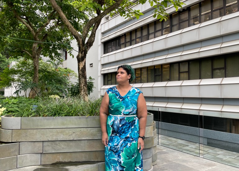 Manisha Wijesinghe, She is in a aquamarine dress standing outside in a courtyard. She has short blue hair.
