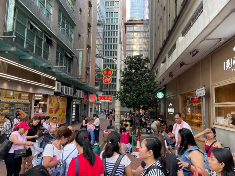 Women gathered on a pedestrianised street in the Central District of Hong Kong. There are high rise buildings on either side.