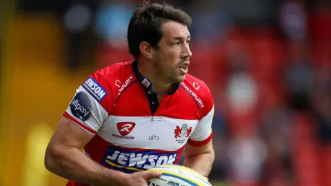 Reuters Tom Voyce playing rugby in a red and white shirt. He's holding the ball and has a mouth guard in.