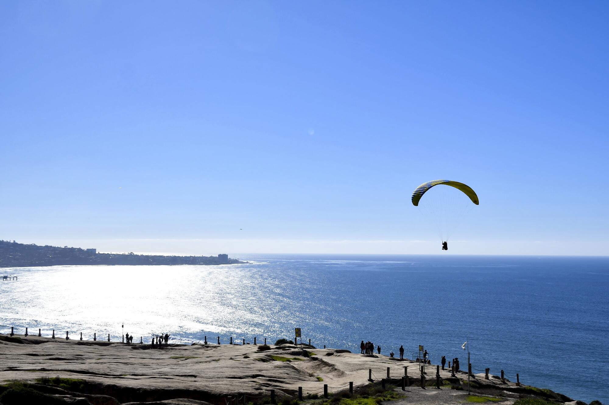 A paraglider glides over the cliffs with an ocean horizon in the background at Torrey Pines Gliderport.