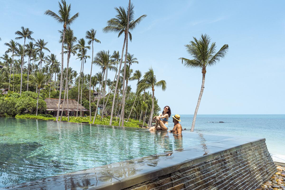 A woman and a man sitting in an infinity pool overlooking a beach and the ocean.