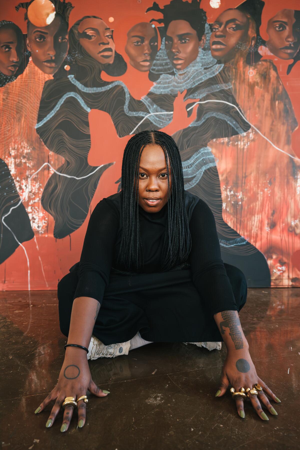 A person crouches on the floor, hands out, in front of a colorful painting
