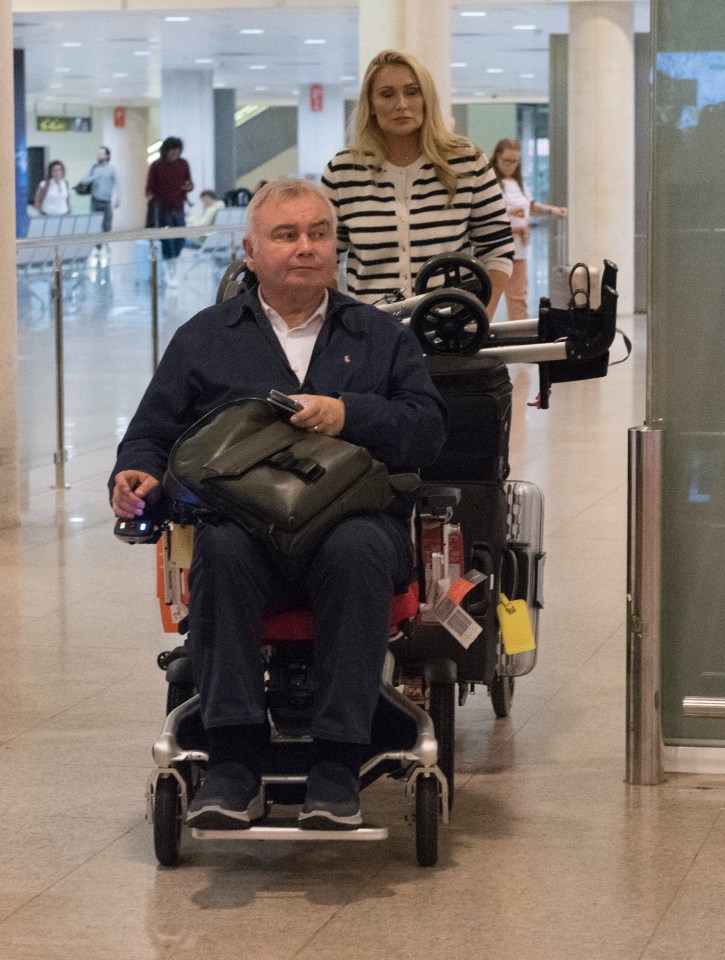Eamonn Holmes in a wheelchair at an airport with his girlfriend.