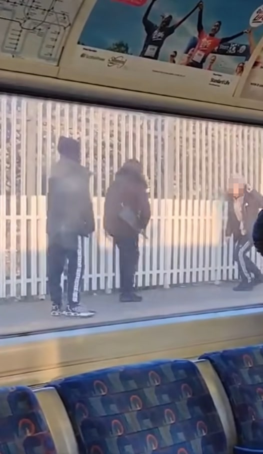 View from a train of four people fighting on a tube station platform.