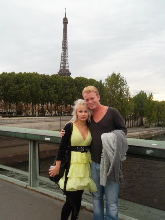 Couple posing on a bridge in Paris with the Eiffel Tower in the background.