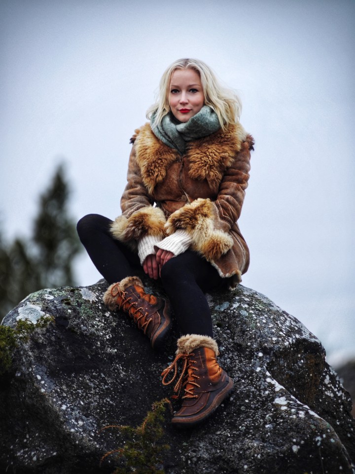 Woman in a fur coat sitting on a rock.