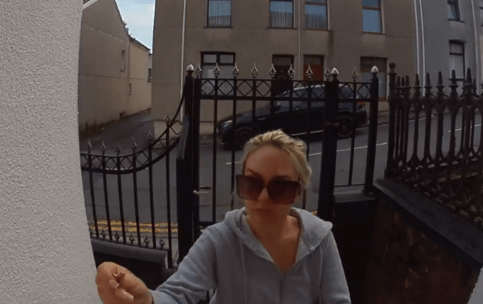 Woman holding a small object outside a house.