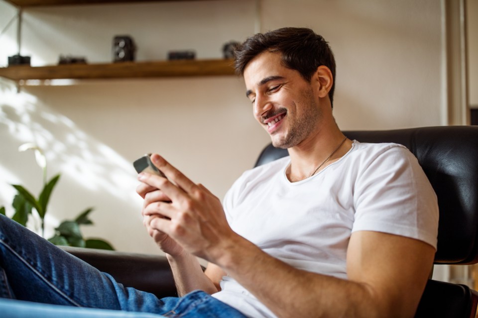 Smiling young man relaxing at home, using his smartphone.