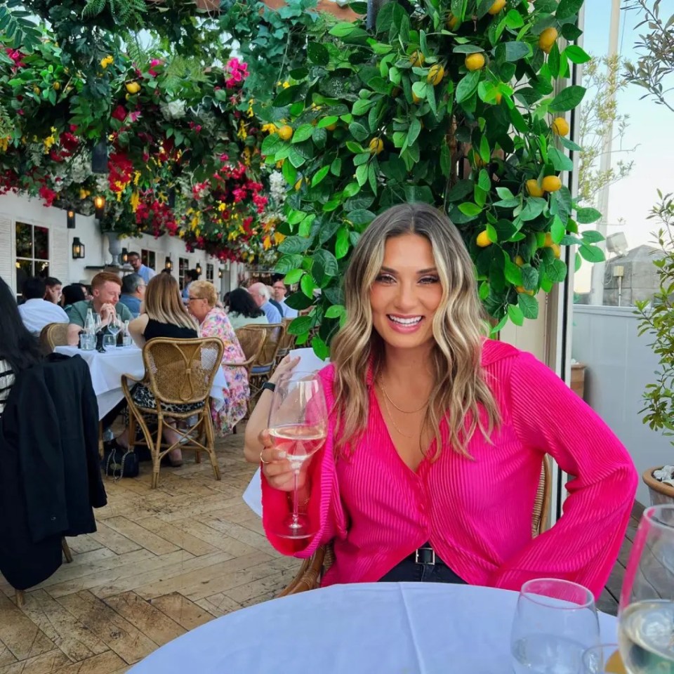 Woman in pink shirt holding a glass of wine at an outdoor restaurant.