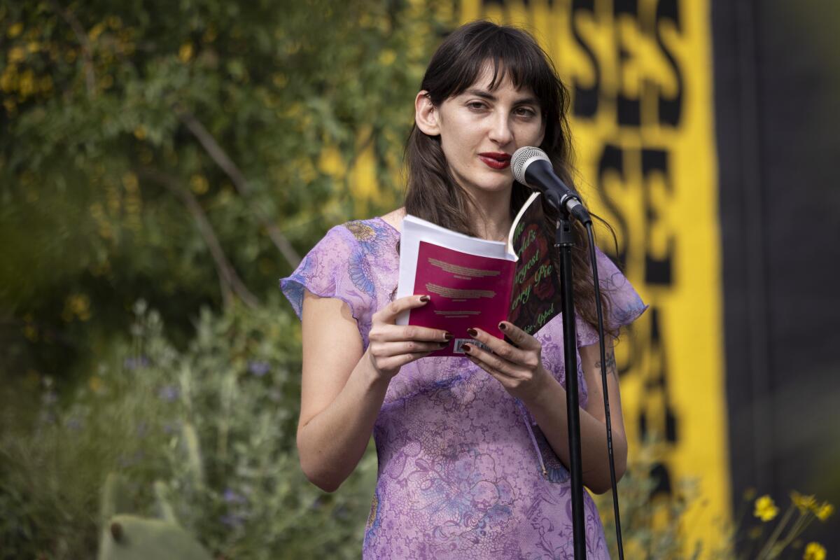 Poet Sophie Appel reads a poem at a microphone during a March 30 book event at 7th Ave Garden