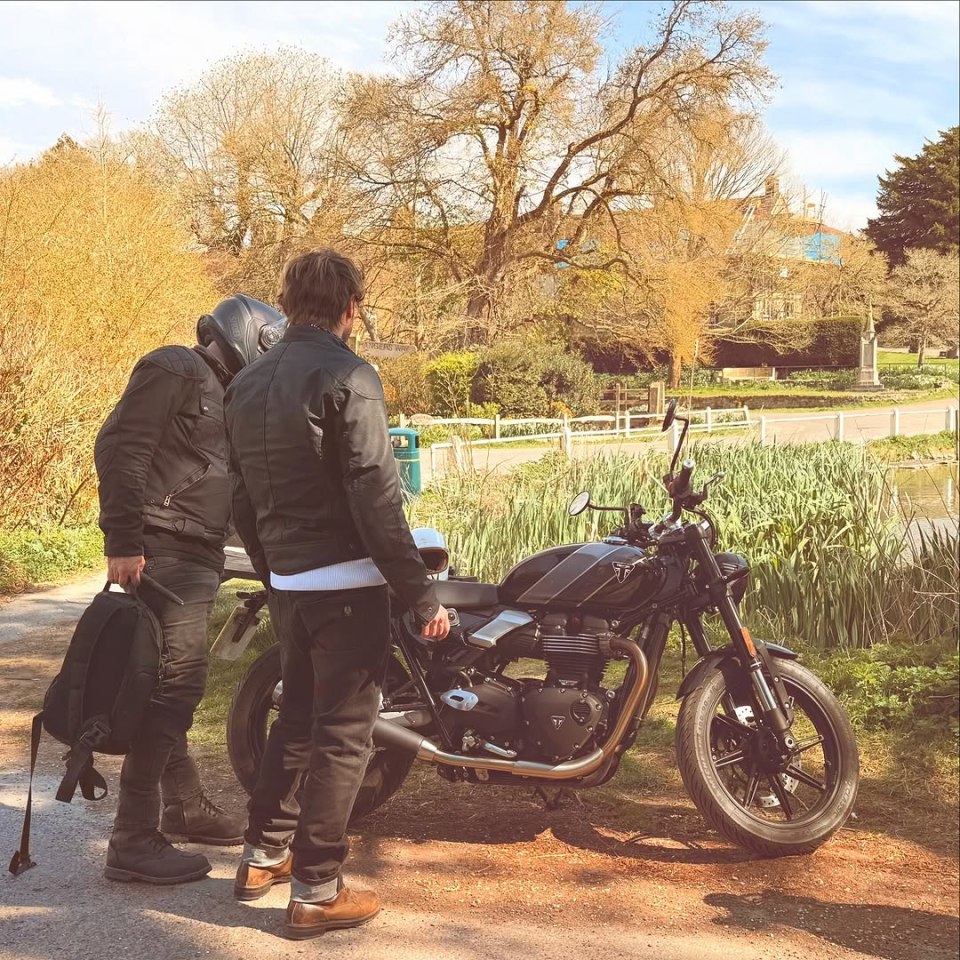 Two men standing near a motorcycle by a pond.