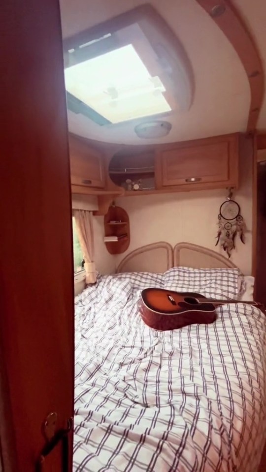 Interior of a small caravan with a bed and acoustic guitar.