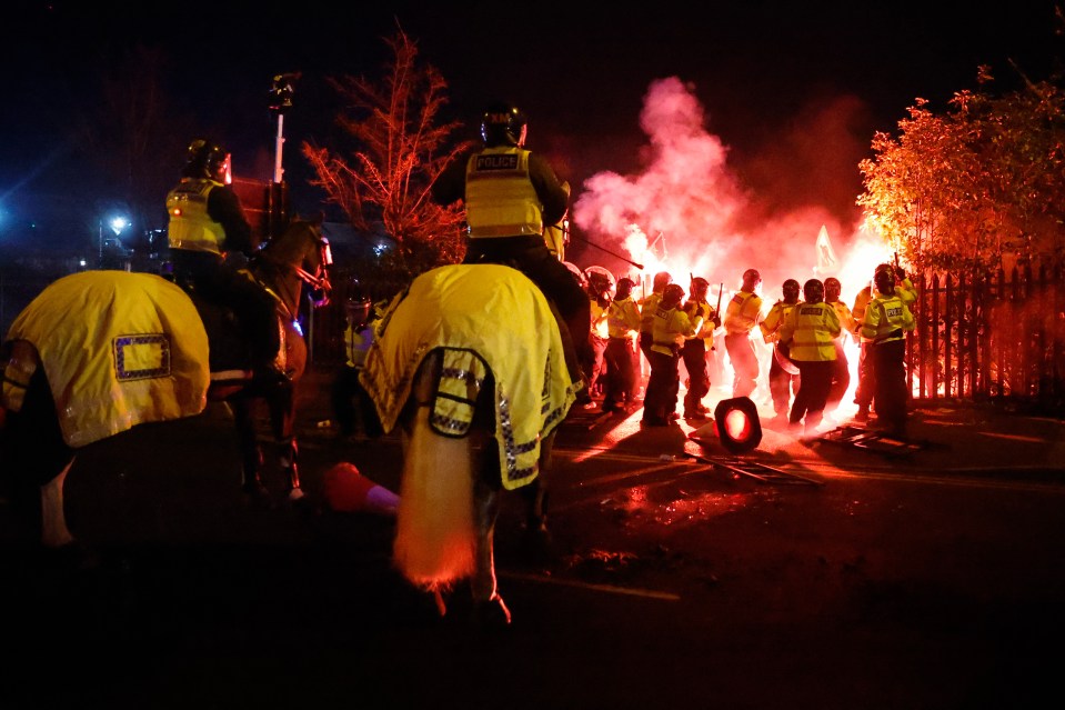 Police on horseback facing a crowd of rioters throwing flares.