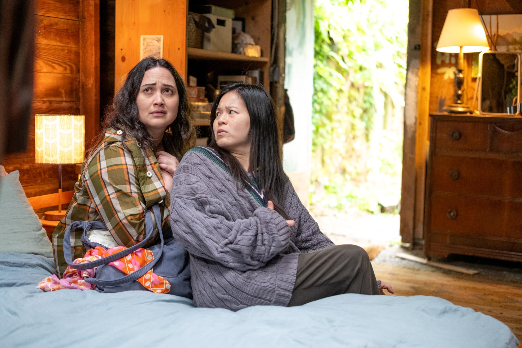 Two women sit on a bed.