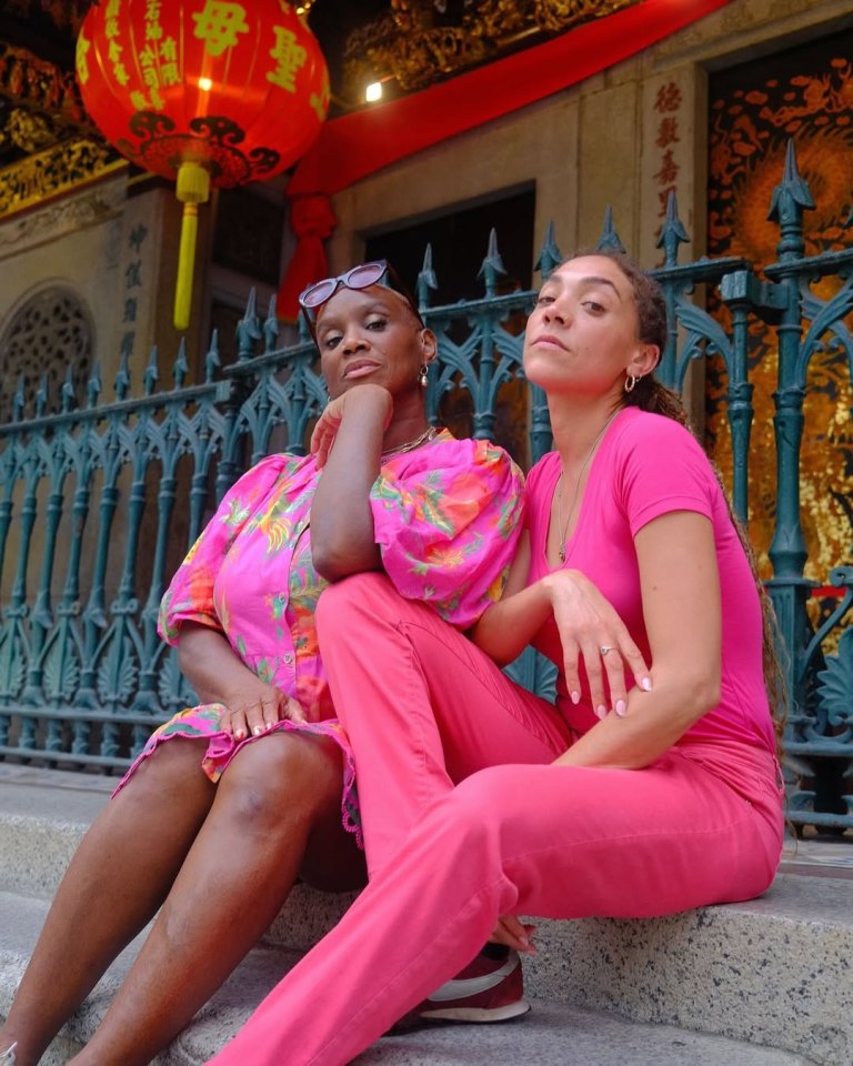 Two women in pink outfits sitting on steps in front of a building.