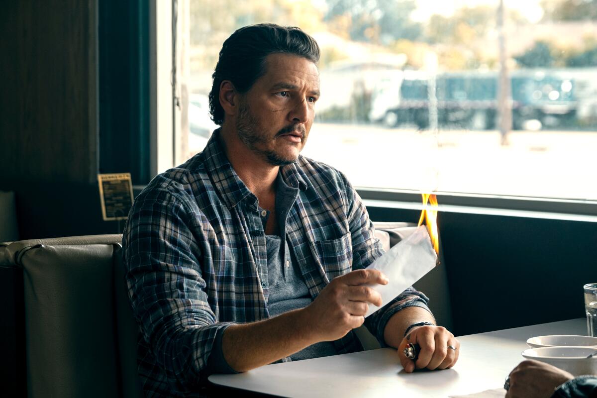A man sits in a diner booth while holding a folded up piece of paper on fire
