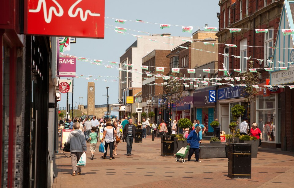 Street scene in Rhyl, Wales, with pedestrians shopping and Welsh flags.