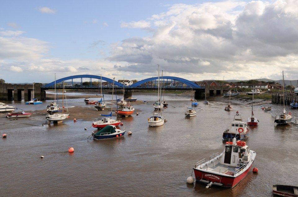 Boats moored in a river estuary under a blue bridge.