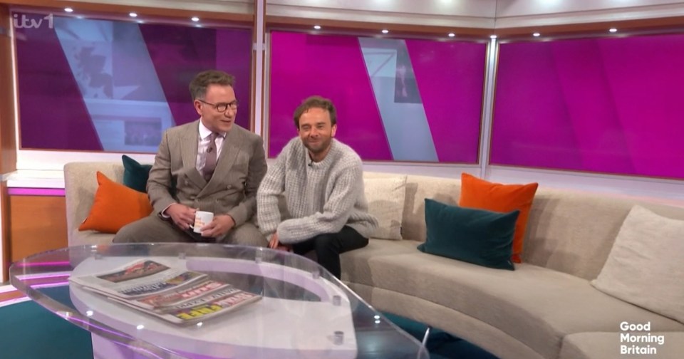 Screenshot of two men sitting on a sofa during a television interview.